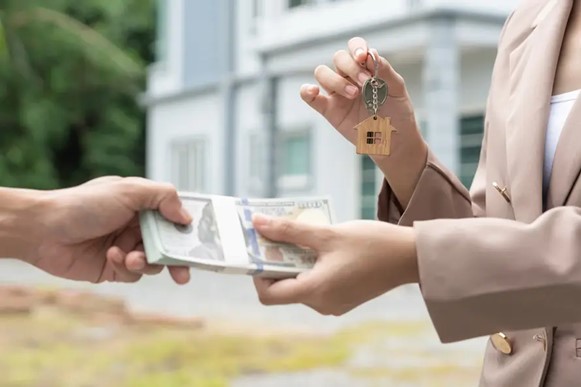 A man hands cash to a woman, illustrating selling a house for cash in Michigan